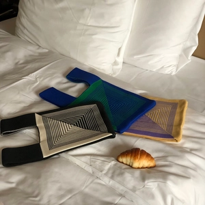 Flat lay of knit tote bags in geometric patterns displayed on white bedding