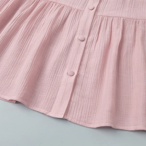 Close-up of pink crepe fabric featuring textured vertical pleats and covered buttons