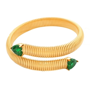 Snake style gold coil bracelet with two green heart shaped crystals on a white background