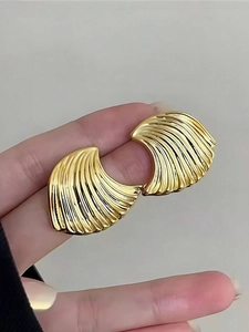 Macro detail of gold earrings featuring radiating wave textures and high metallic luster