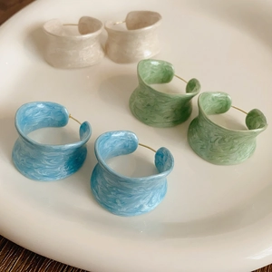 Detail view of retro C-shaped earrings with marble texture in beige, green, and blue hues