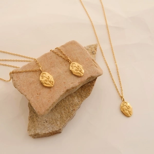 Close-up of gold rose engraved oval pendant necklace on stone background