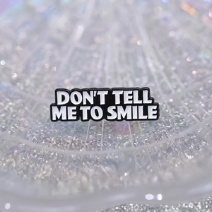 Black and white enamel pin featuring the text DON'T TELL ME TO SMILE on shiny background