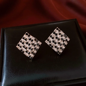 Detail of square checkered earrings with black and white zircon on black leather
