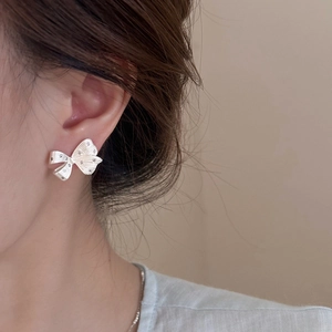 Close-up of a silver bow earring with textured finish on model's ear, stylish and elegant
