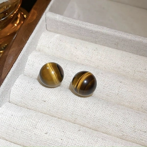 Macro shot of tiger eye stone earrings on a beige velvet tray inside a wooden box