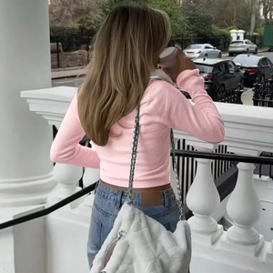 Detail of pink slim-fit cropped cardigan styled with denim jeans and white chain bag