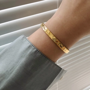 Macro view of gold 18K plated stainless steel bangle with lunar irregular hammered texture