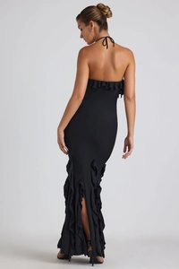 Détail de la robe dos nu à licou avec volants et une fente haute sur tissu noir élégant