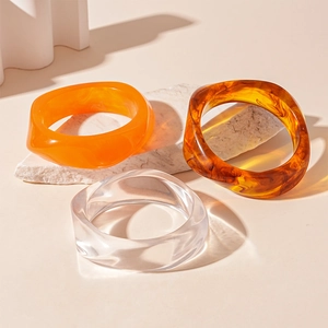 Irregular acrylic resin bangles in orange, amber, and clear finishes on stone display