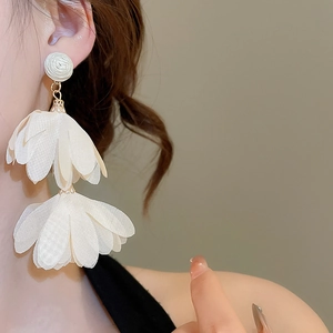 Close-up of white chiffon flower tassel earrings worn by a model in soft lighting