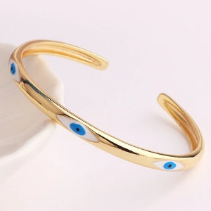 Nahaufnahme der goldenen Evil Eye Manschette mit blauer Emaille auf rosa Hintergrund