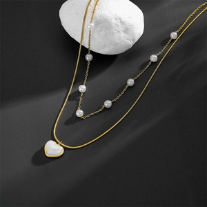 Close-up of double-layer gold necklace featuring white pearls and a white heart pendant
