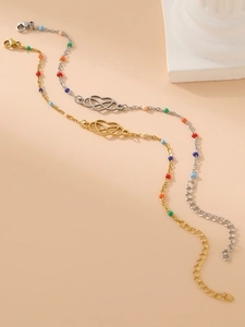 Detailed close-up of 18k gold heart Mobius bracelet with colorful beads on a beige background