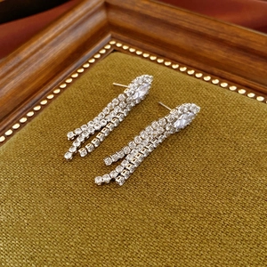Detailed view of silver zircon tassel earrings on a textured green fabric background