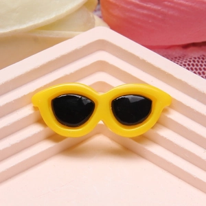 Close-up of a miniature yellow resin sunglasses charm on a pink tiered display stand