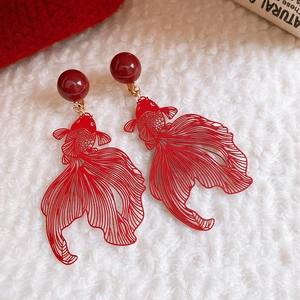 Detail of red hollow goldfish earrings with beads on a soft white faux fur background