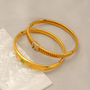 Detail view of two gold titanium steel bangles with colorful zircons and spiral texture