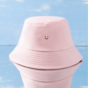 Pink cotton bucket hat featuring a black smiley face print on a light blue wood background