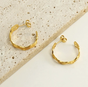Detailed close-up of golden wavy twisted hoop earrings on a textured stone display