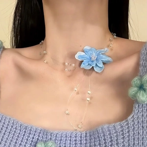 Gros plan détaillé d'un pendentif fleur bleue sur un collier en fil de pêche perlé