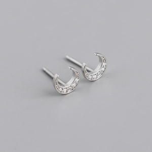 Macro shot of silver crescent moon earrings with inlaid zircons on a gray background