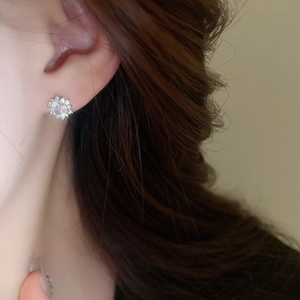 Detail shot of a sparkling zircon snowflake earring worn on a model's earlobe