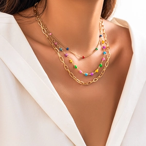 Close-up of triple-layered gold necklaces with colorful beads and heart pendants