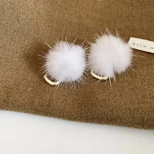 Close-up of white plush pompom earrings with gold U-shaped metal clips on fabric