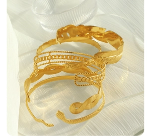 Macro detail of 18K gold plated Cuban link and leaf texture bracelet set on white fabric