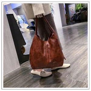Close-up of a large vintage brown faux leather tote bag held by a model in a street setting