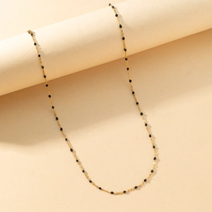 Close-up of a delicate golden necklace chain with small black circular beads on a pedestal