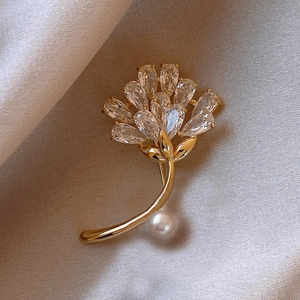 Detail of golden leaf brooch with sparkling crystals and a white pearl on silk fabric