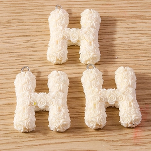Macro detail of resin letter H pendants featuring 3D white rose flower textures and metal rings