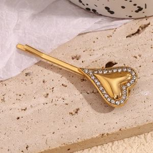 Macro shot of gold-plated heart hair clip with sparkling diamonds on textured stone surface