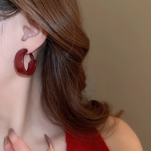 Close-up of deep red glossy hoop earring worn by a model in a warm-toned setting