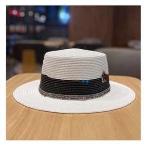 Dettaglio cappello di paglia bianco a tesa piatta con nastro nero e spilla a fiore