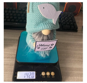 Detail shot of a knitted gnome doll on an electronic scale showing product weight