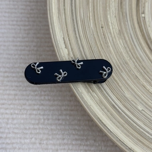 Close-up of black rectangular hair clip with silver metal bow accents on wooden tray