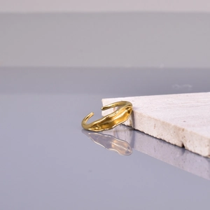 Irregular wave-shaped gold open ring on a beige stone base with elegant reflection