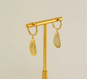 Macro shot of gold hoop earrings with hollow wing pendants on a golden T-shaped display