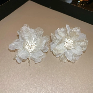 Detail of elegant cream organza flower earrings with pearl centers on leather background