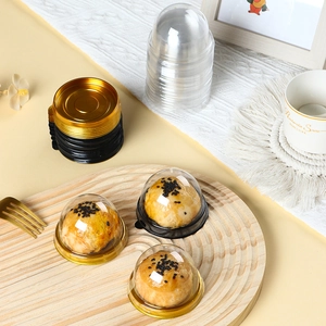 Clear round plastic mooncake boxes with gold bases for pastries shown on a wooden tray
