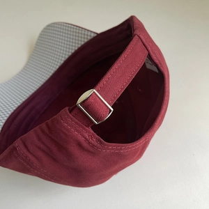Detailed macro view of the burgundy cotton baseball cap with adjustable metal buckle strap
