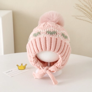 Close-up of pink knit baby hat featuring plush pom-pom and green heart pattern details