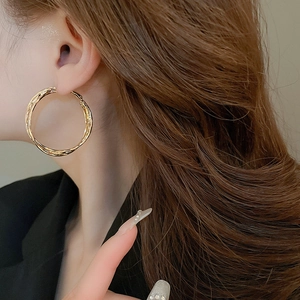 Close-up of gold layered twisted hoop earrings worn on a model's ear for a chic look