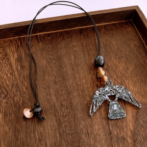 Détail du collier pendentif oiseau à motif marbre avec perles sur plateau en bois