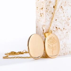 Golden oval rose engraved locket necklace on stone, showing interior photo slot