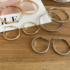 Detailed view of textured gold and silver hoop earrings in two sizes on wooden surface
