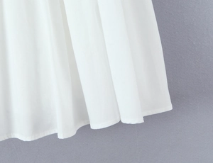 Detailed macro view of white mini dress hem with pleated fabric and fine stitching